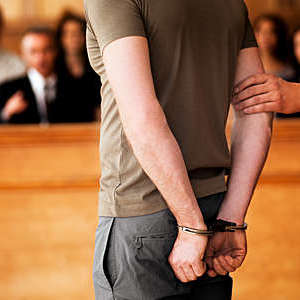 Handcuffed man standing in courtroom. 