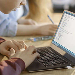 Hands of a young boy working on a laptop. 