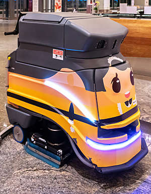 Robot cleaning vehicle with yellow body and cartoonish face photographed in Singapore's Changi Airport.