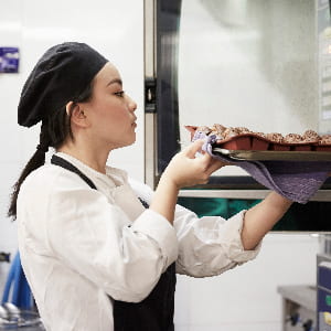 Side view of female chef taking out tray of cookies from oven at commercial kitchen.