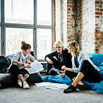 Three businesswomen hold an informal meeting sitting on comfy bean bag cushions at the office.