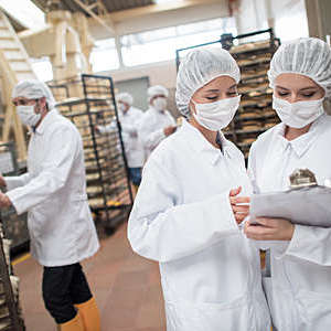 Women working at a food factory and looking at checklist on a clipboard.