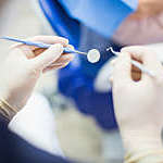 Close up of the hands of a dentist with surgical gloves and tools in hand.