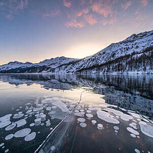 Piz Da La Margna mirrored in the frozen Lake Sils covered of ice bubbles, canton of Graubunden, Switzerland.