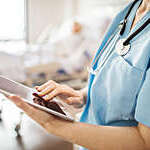 Midsection of female nurse using digital tablet in hospital. Close-up of medical professional is touching screen in ward. She is wearing scrubs.